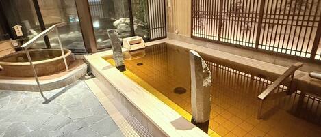 Un onsen japonais traditionnel, avec un sol en pierre, des bancs en bois et un espace de baignade carrelé.