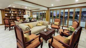 Un amplio vestíbulo de hotel con un sofá grande, varios sillones, una estantería y un ventanal con vistas al exterior.