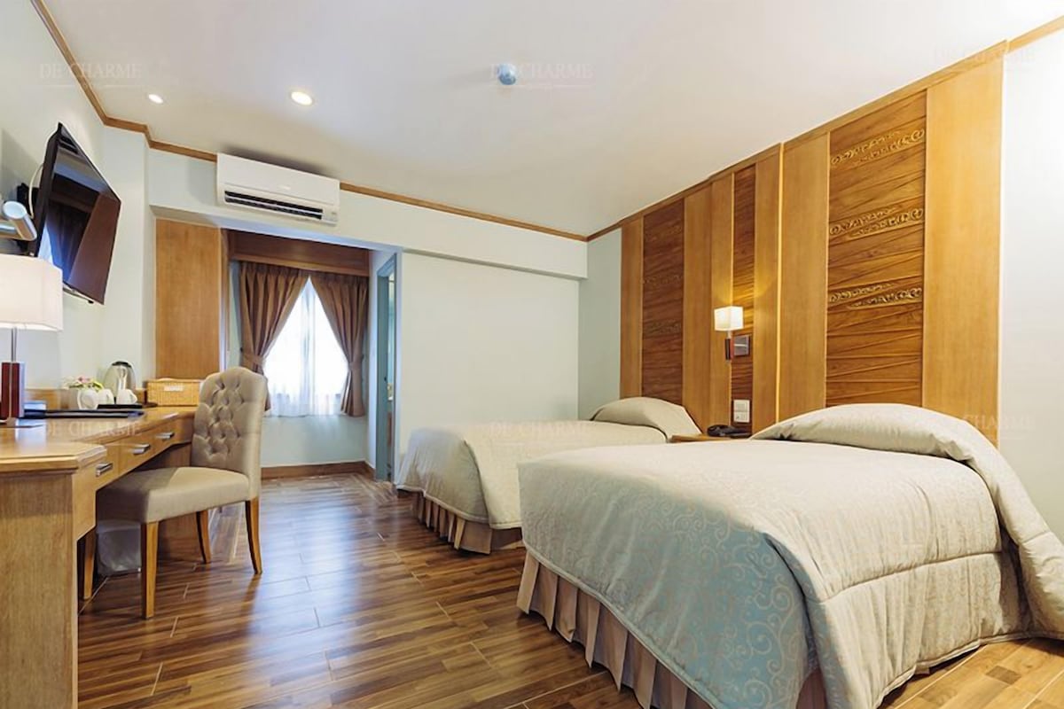 Une chambre d’hôtel avec un bureau en bois, deux lits, une chaise et un appareil de climatisation.