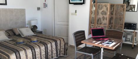 A bedroom with a bed, a desk with a laptop, a chair, a coffee machine, and a decorative screen.