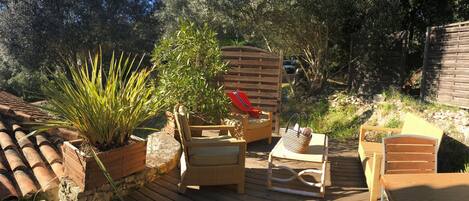 Un patio al aire libre con piso de madera, mobiliario de mimbre y plantas en macetas.