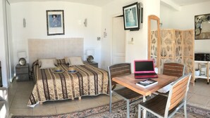 A bedroom with a bed, bedside table, lamp, and a laptop on a wooden table.