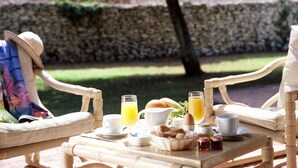 A wicker table set with breakfast items, including eggs, toast, and orange juice, in an outdoor setting with stone walls and greenery in the background.