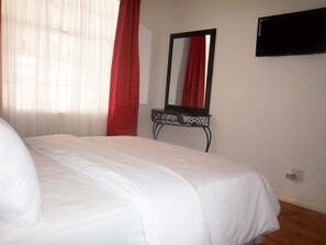 Una cama bien tendida en una habitación con un espejo grande en la pared y una mesita de noche.