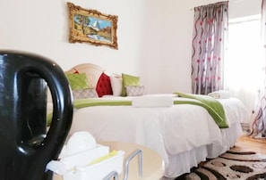 Una habitación de hotel con una cama, una silla, una mesita con una bandeja y un cuadro en la pared.