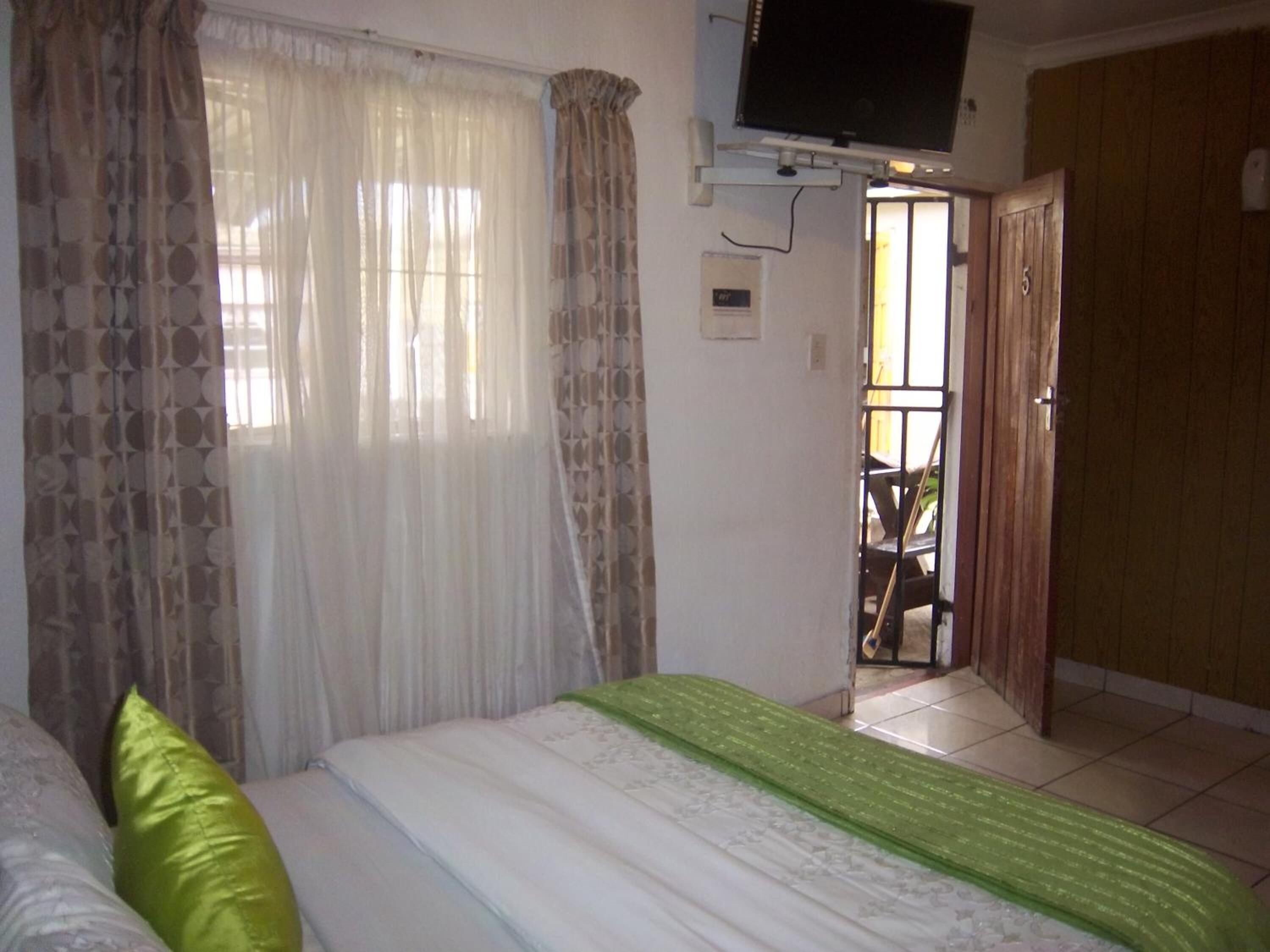 Une chambre à coucher comprenant un lit, des rideaux, une télévision et une porte donnant sur un balcon.