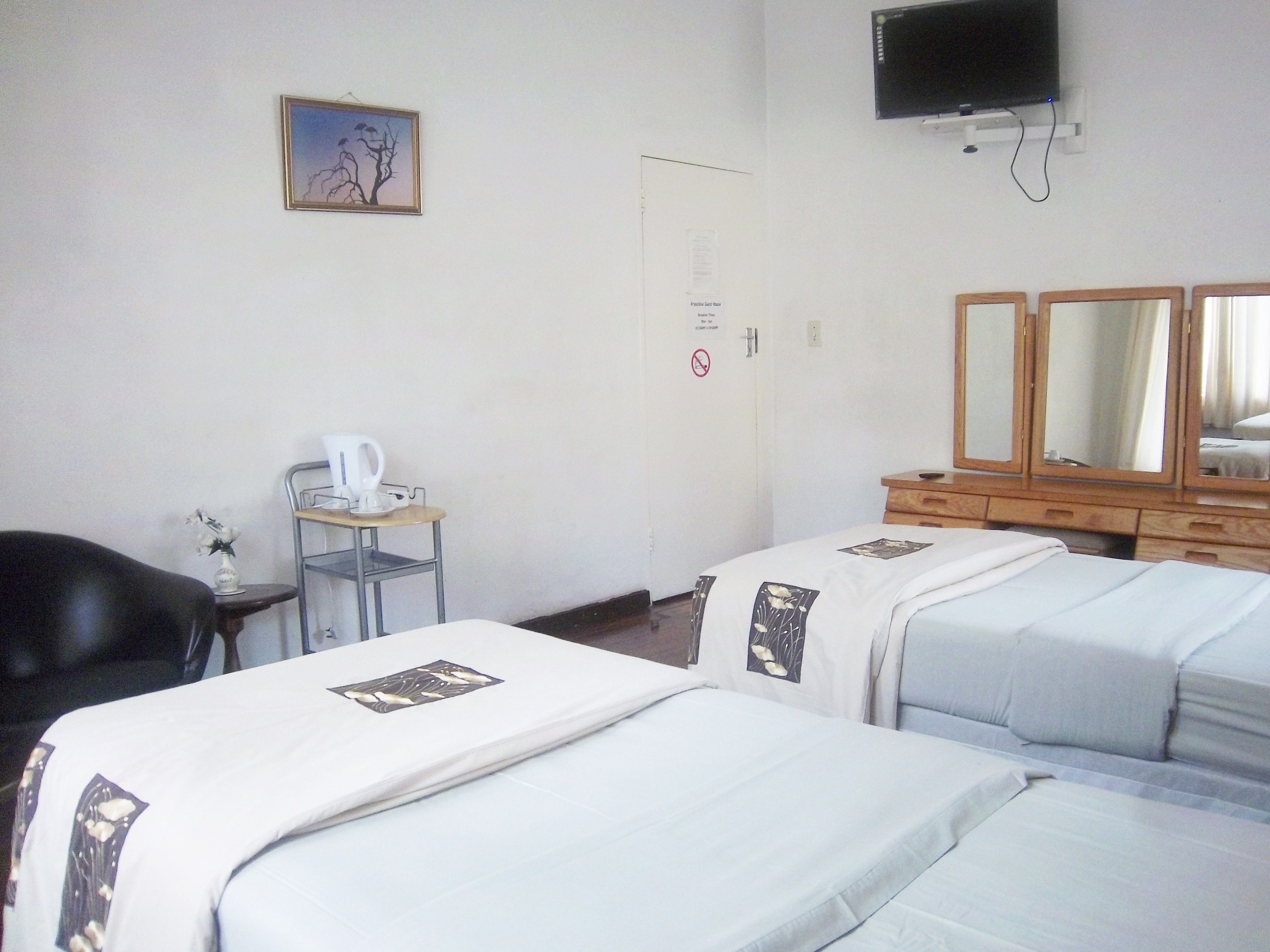Une chambre d’hôtel avec deux lits, un bureau avec une chaise, un téléviseur fixé au mur et une porte avec une pancarte.