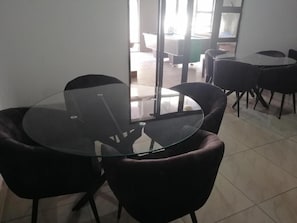 Un salón de conferencias con una mesa de vidrio rodeada de sillas, una mesa de billar al fondo y vistas al exterior a través de un ventanal.