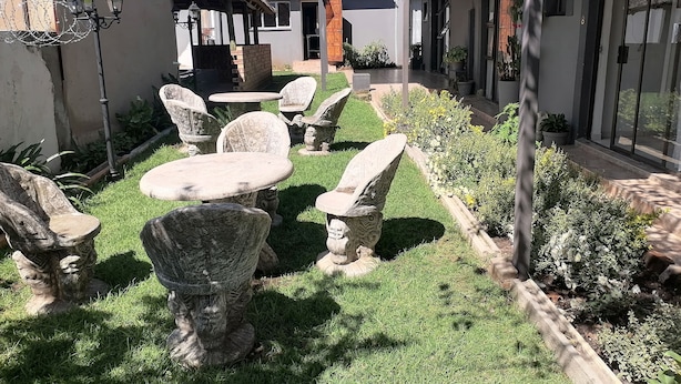 Une cour avec des meubles en pierre, une structure dotée d’un toit de chaume et un jardin bien entretenu.