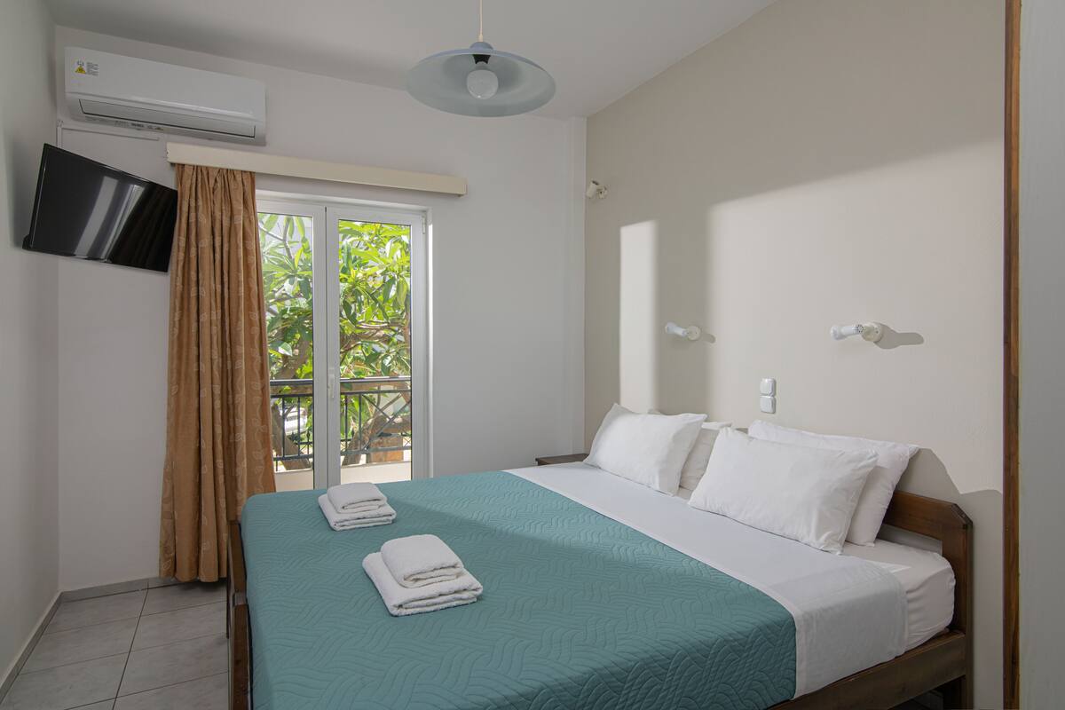 A hotel room with a bed, a TV mounted on the wall, and an air conditioning unit.