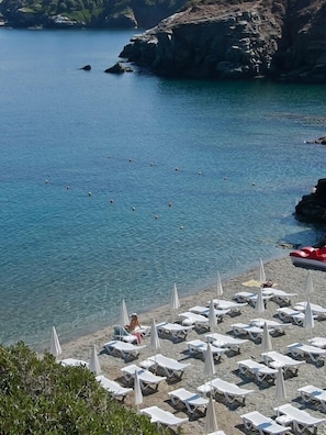A beach with clear blue water, rocky cliffs, and sun loungers. - Litsa Mare apartments (Malevizi)