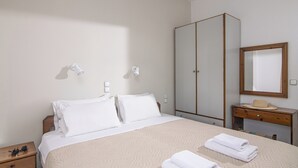 A hotel room with a bed, bedside tables, a wardrobe, a vanity with a mirror, and a wall-mounted light fixture. - Litsa Mare apartments (Malevizi)