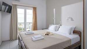 A hotel room with a bed, a TV, a balcony, and a window with curtains. - Litsa Mare apartments (Malevizi)