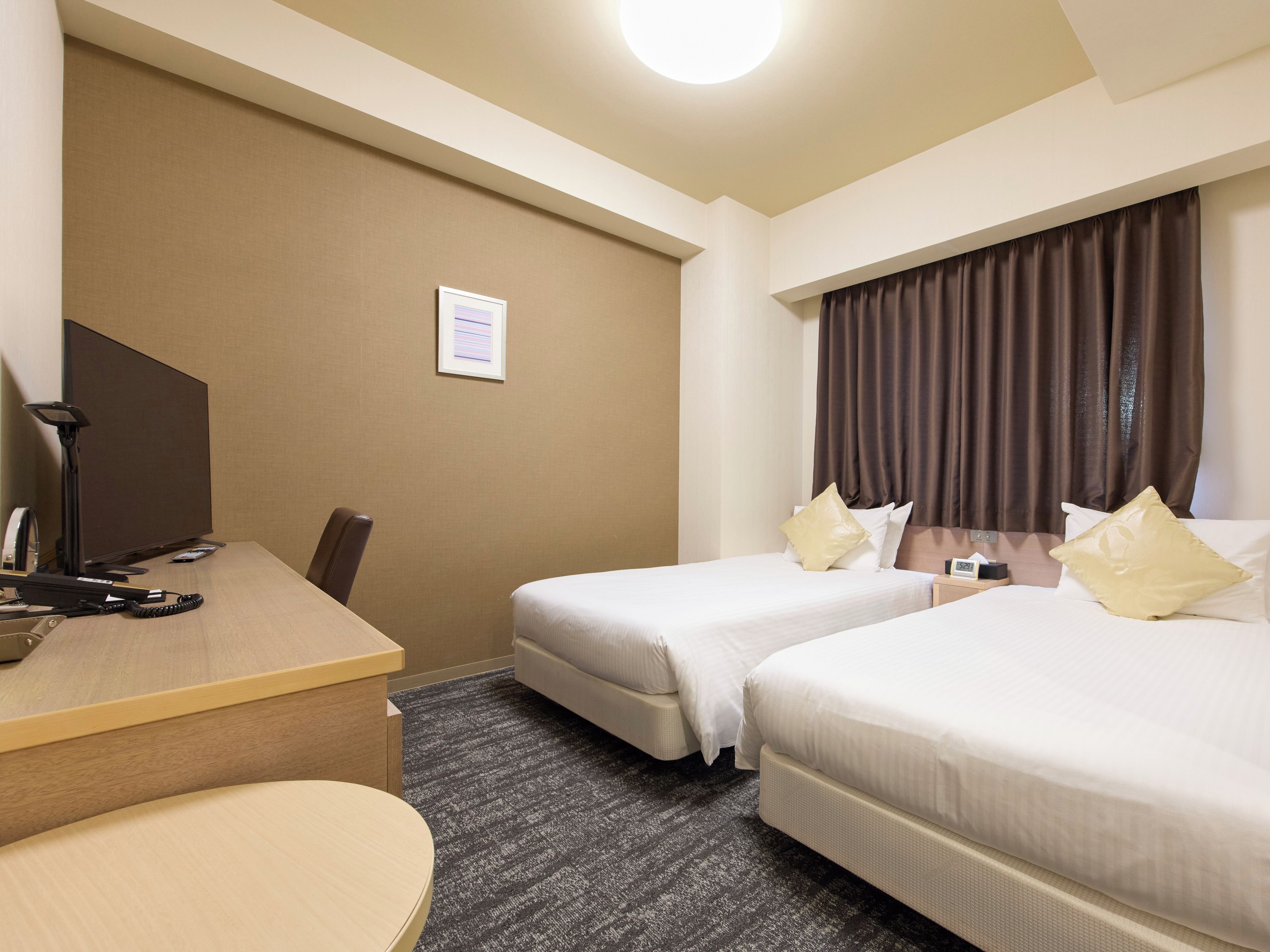 A hotel room with two beds, a desk, and a chair.
