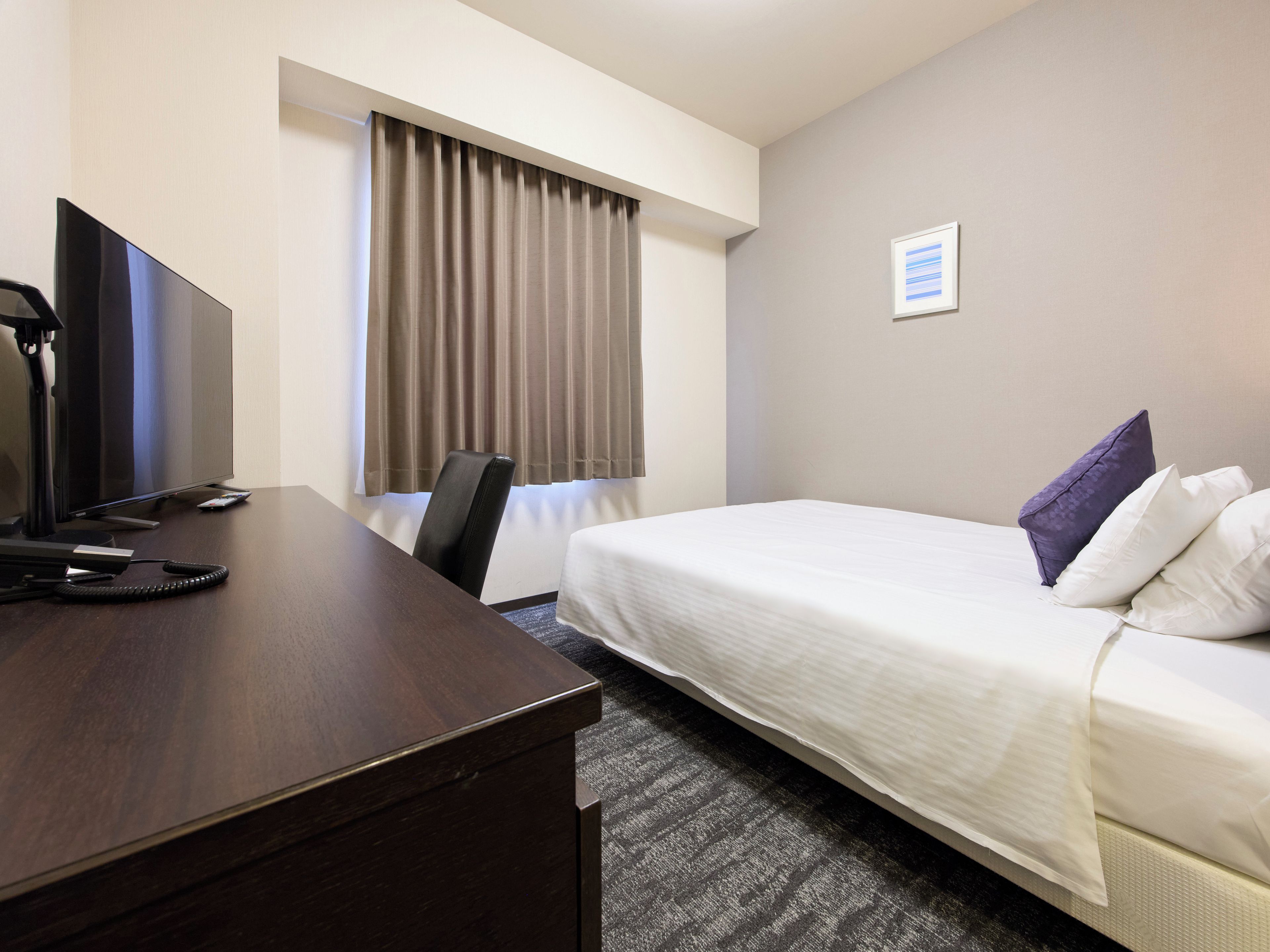 Una habitación de hotel con una cama, un escritorio con ordenador, una silla y una ventana con cortinas.