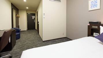 Una habitación de hotel con cama, escritorio con silla, un pequeño sofá y una mesita de noche con lámpara.