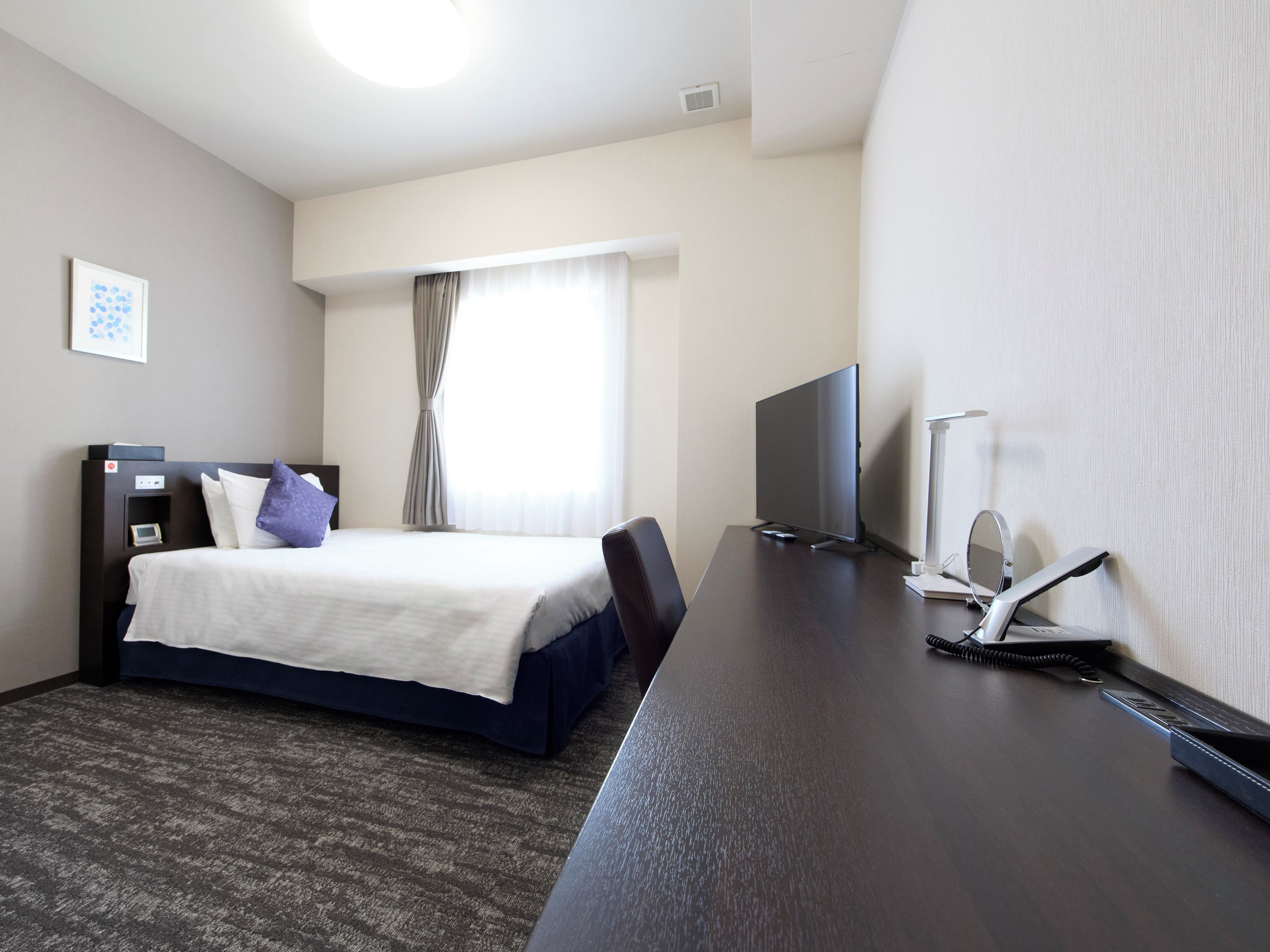 A hotel room with a bed, a desk, a television, and a window with curtains.