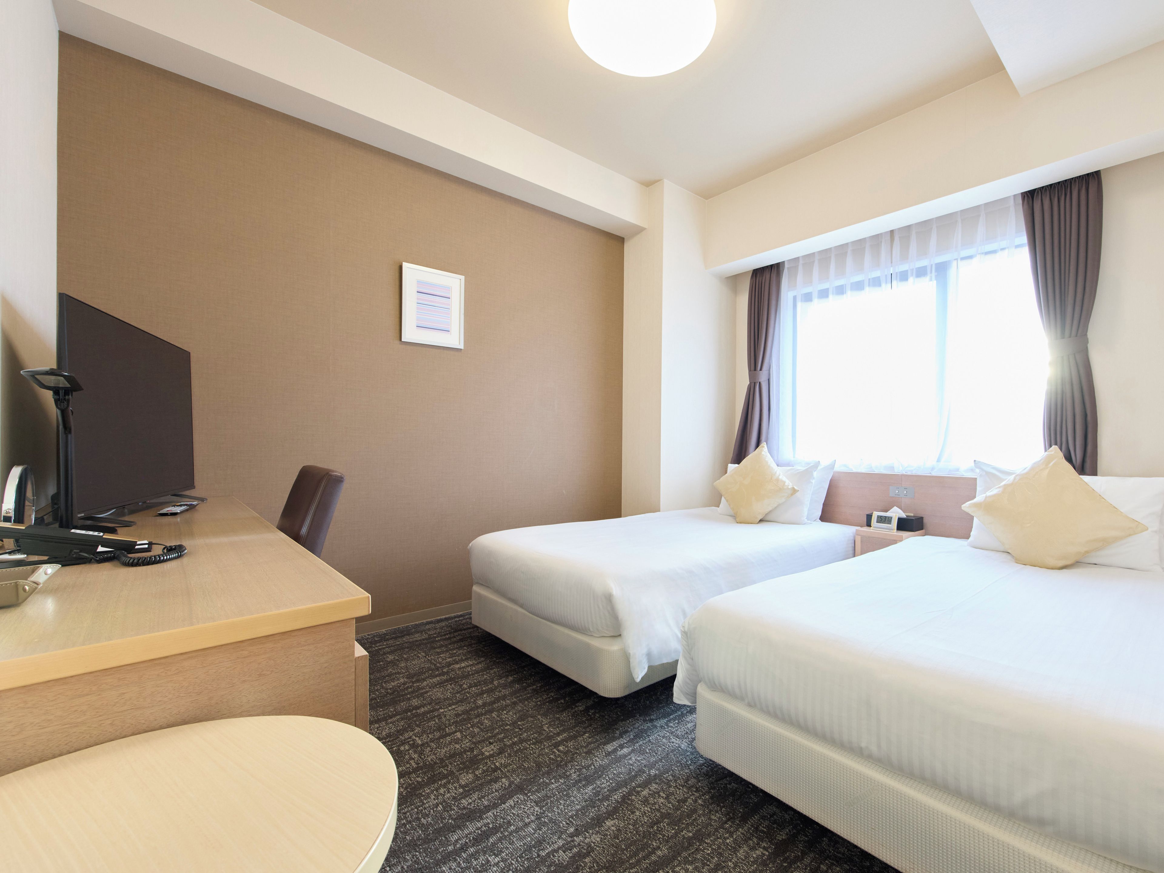 Habitación de hotel con escritorio, dos camas, una silla, televisor de pantalla plana y ventana con cortinas.