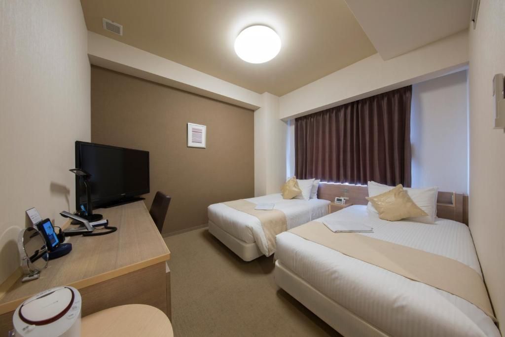 Une chambre d’hôtel avec deux lits, un bureau avec une télévision et une fenêtre avec des rideaux.