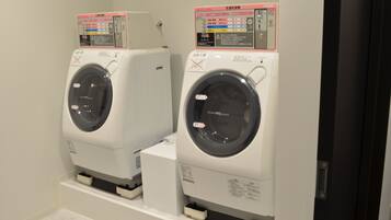 Two front-loading washing machines with control panels, placed side by side in a room with white walls and a tiled floor.