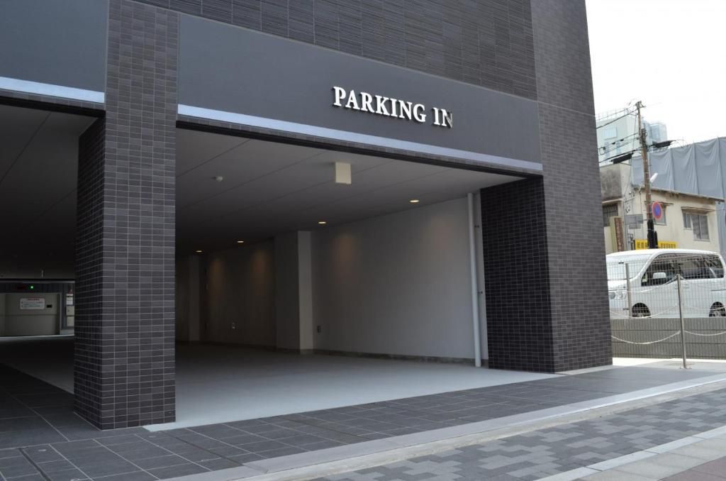 A building entrance with a 'PARKING IN' sign, a gated parking area, and a white van parked outside.