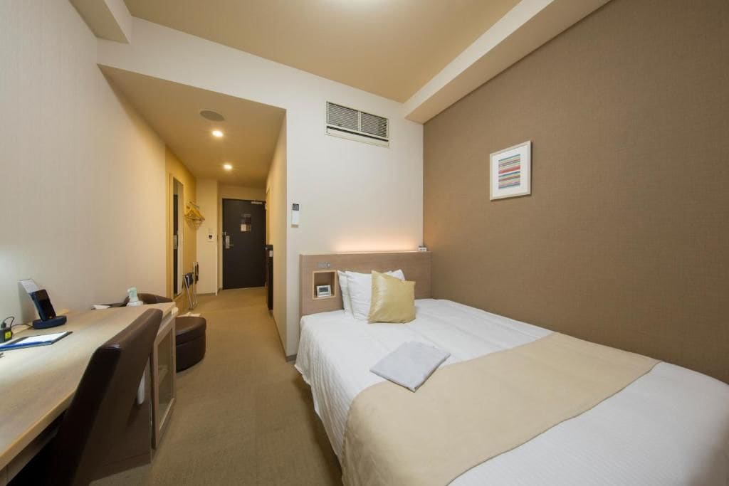 Una habitación de hotel con cama, escritorio con silla, mesita pequeña y mesita de noche.