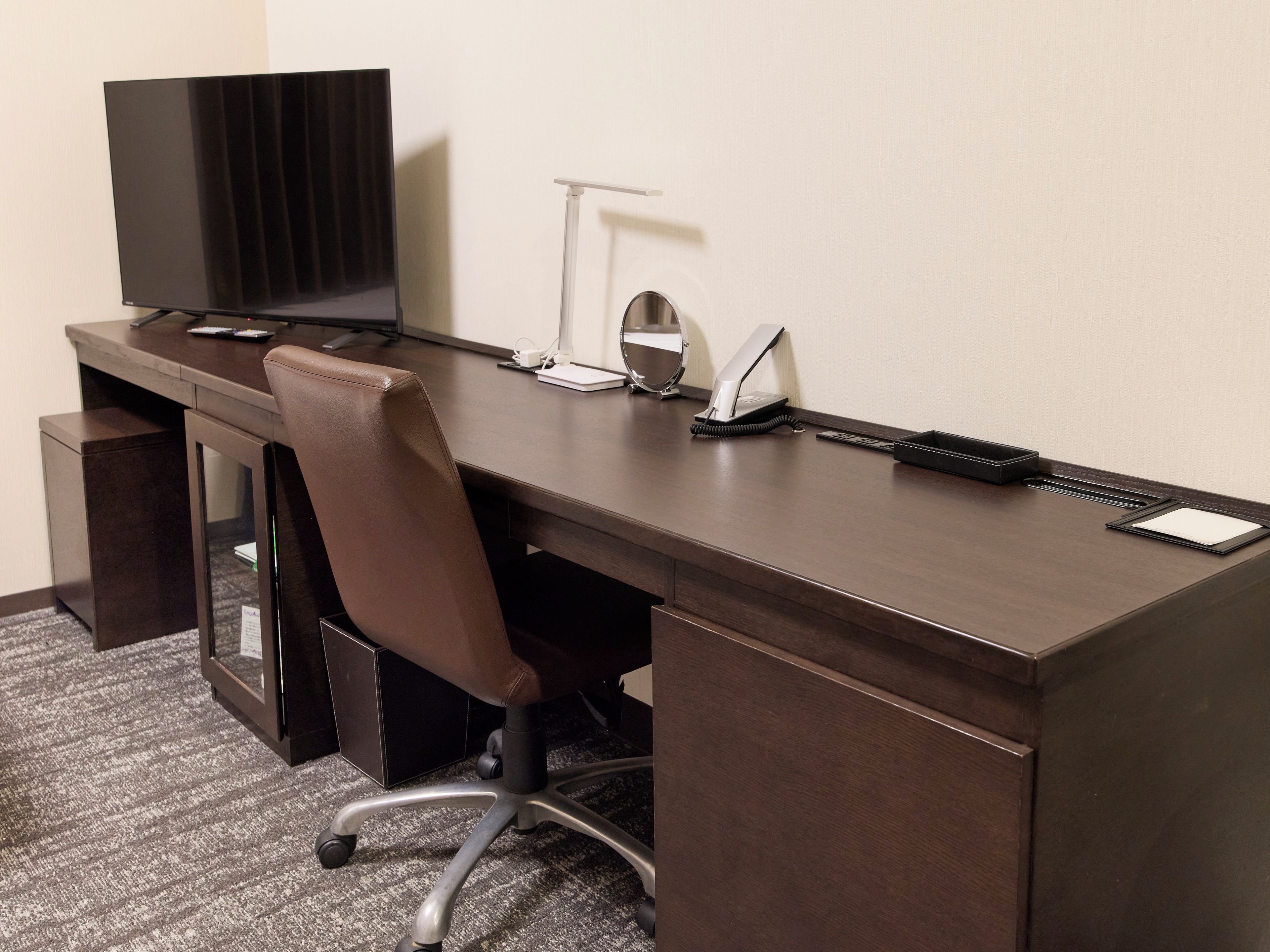A hotel office desk with a computer, telephone, and desk lamp.
