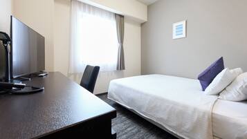Een hotelkamer met een bed, een bureau met een computer, een stoel en een raam met gordijnen.