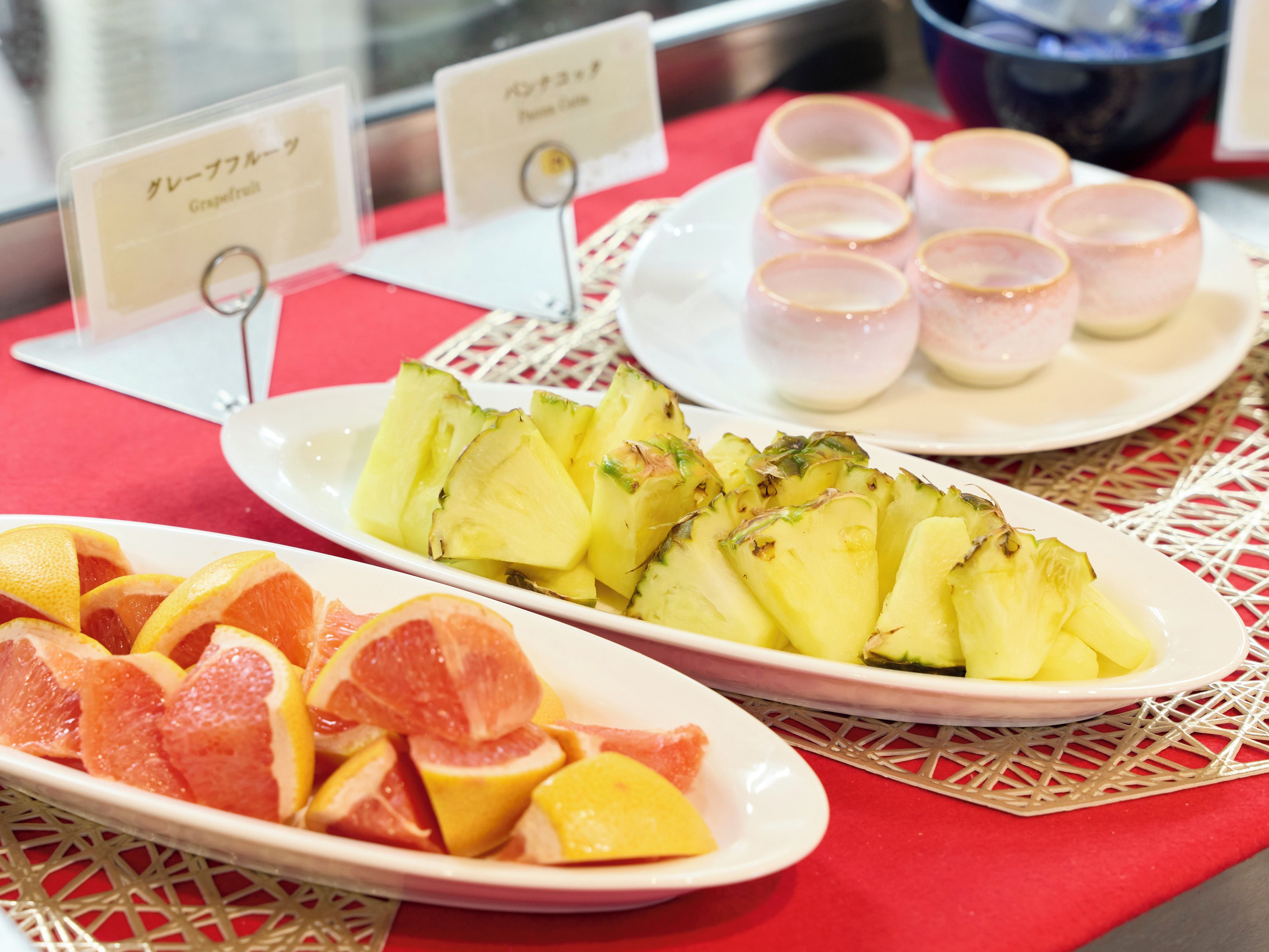 A table with plates of sliced fruits and small cups, likely for a breakfast or snack setting.