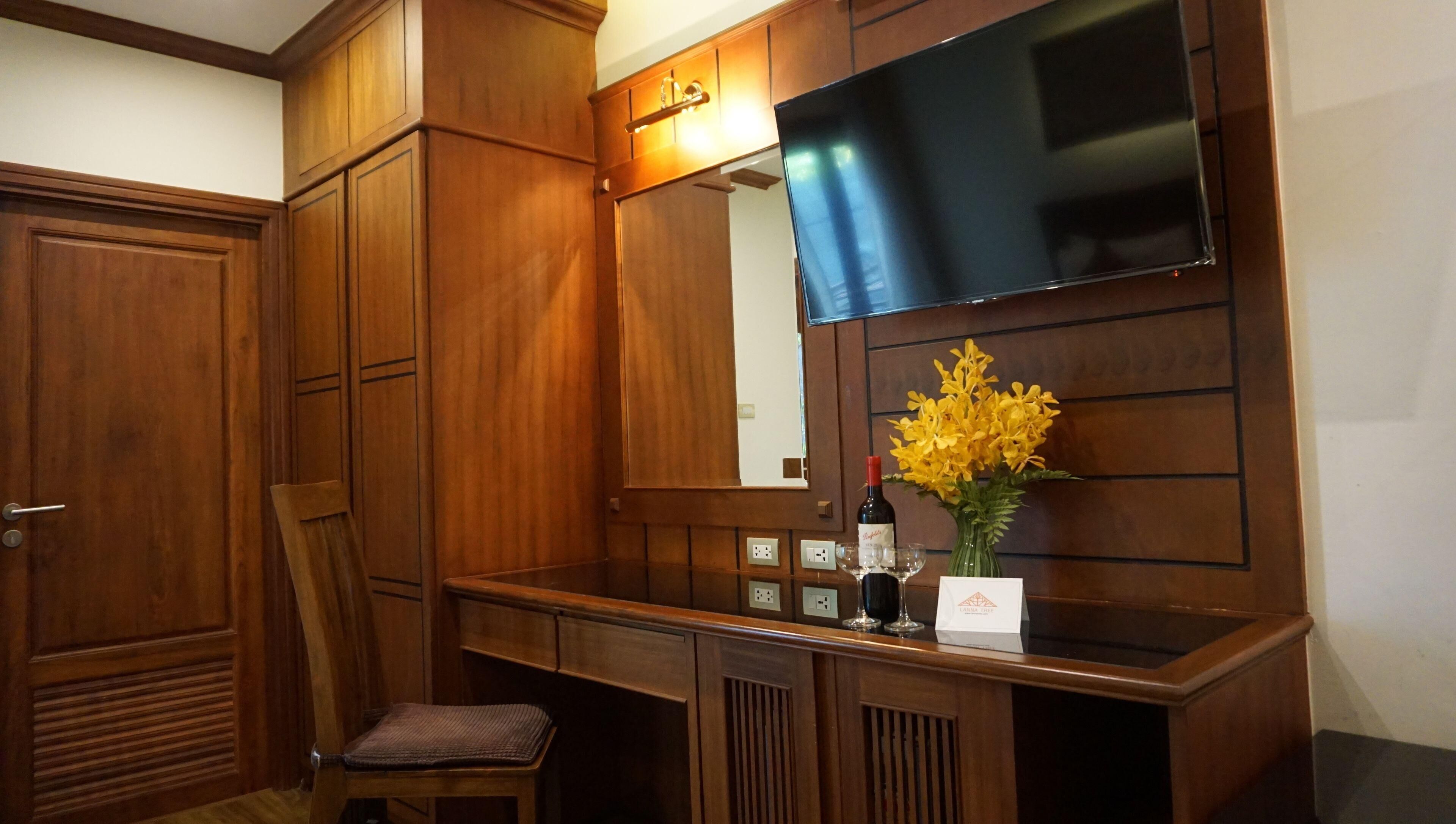 A wooden vanity with a mirror, a chair, a vase with yellow flowers, and a wine bottle.