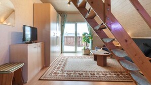 A cozy living room with a wooden staircase, a television, a sofa, and a dining area. - Gasthaus Falkenhain (Altenberg)