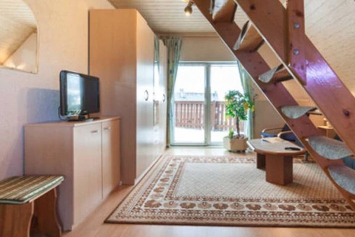 A cozy living room with a wooden staircase, a television, a sofa, and a dining area.