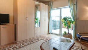 A room with a large wardrobe, a television, a table with a remote, and a view of the outside through a sliding door. - Gasthaus Falkenhain (Altenberg)