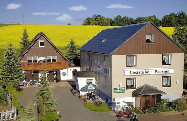 A building with a sign reading "Gaststube - Pension" adjacent to a smaller structure with a balcony. - Gasthaus Falkenhain (Altenberg)