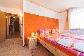 A bedroom with a wooden bed, orange headboard, and a window with curtains. - Gasthaus Falkenhain (Altenberg)