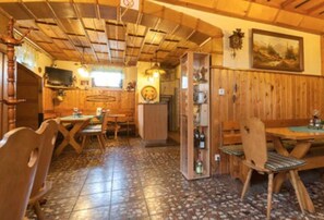 A rustic interior with wooden walls and floors, a dining area with wooden chairs and tables, and a kitchen area with a stove and cabinets. - Gasthaus Falkenhain (Altenberg)