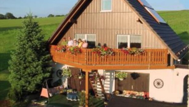 A wooden house with a balcony, a garage, and a large tree in the yard. - Gasthaus Falkenhain (Altenberg)