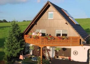 A wooden house with a balcony, a garage, and a large tree in the yard. - Gasthaus Falkenhain (Altenberg)