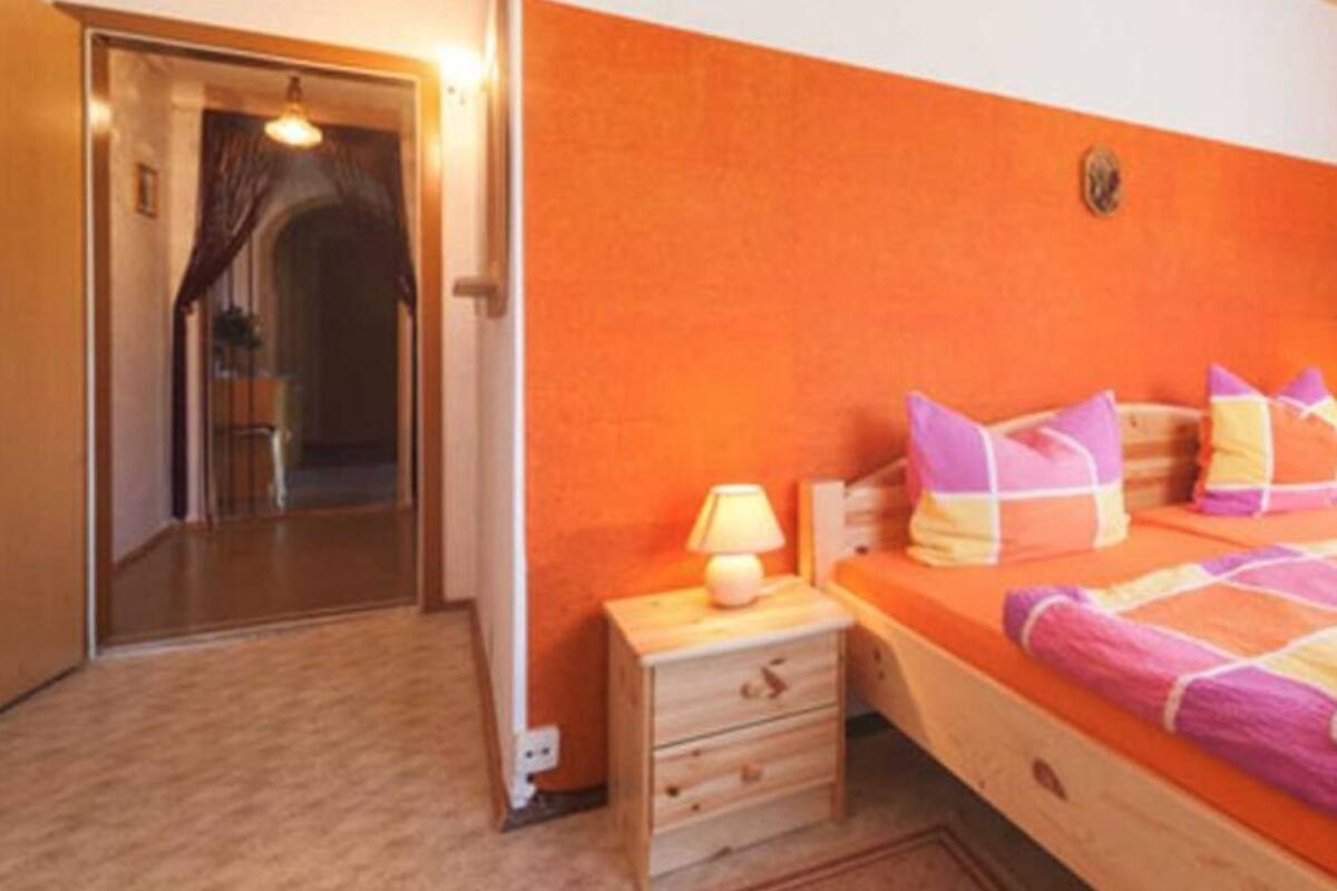 A bedroom with a bed, bedside table, lamp, and a door leading to another room.