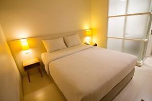 A neatly made bed in a hotel room with a headboard, two bedside lamps, and a small nightstand.