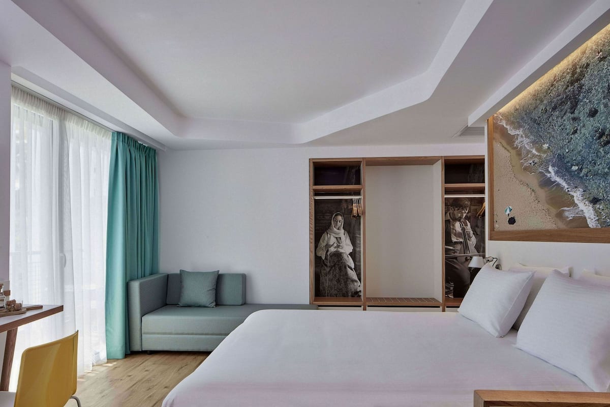 Une chambre d’hôtel moderne dotée d’un grand lit, d’un coin salon avec des coussins, d’une armoire et d’une œuvre d’art accrochée au mur.