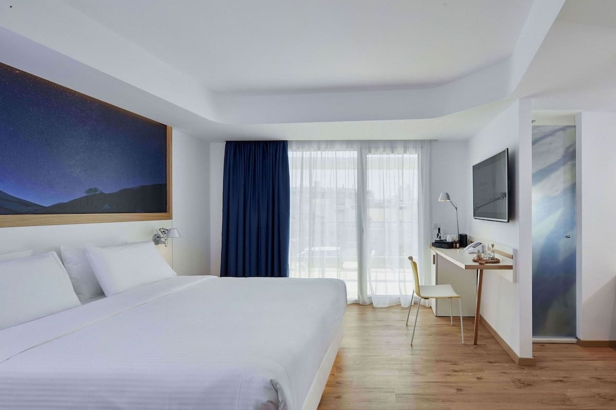 Une chambre d’hôtel avec un lit, un bureau, une chaise, une télévision et un tableau au mur.