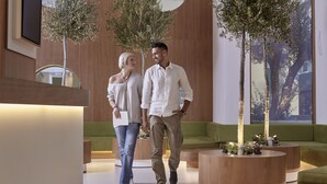 Un hall d’entrée moderne avec un comptoir d’accueil en bois, des sièges verts et des plantes d’intérieur.
