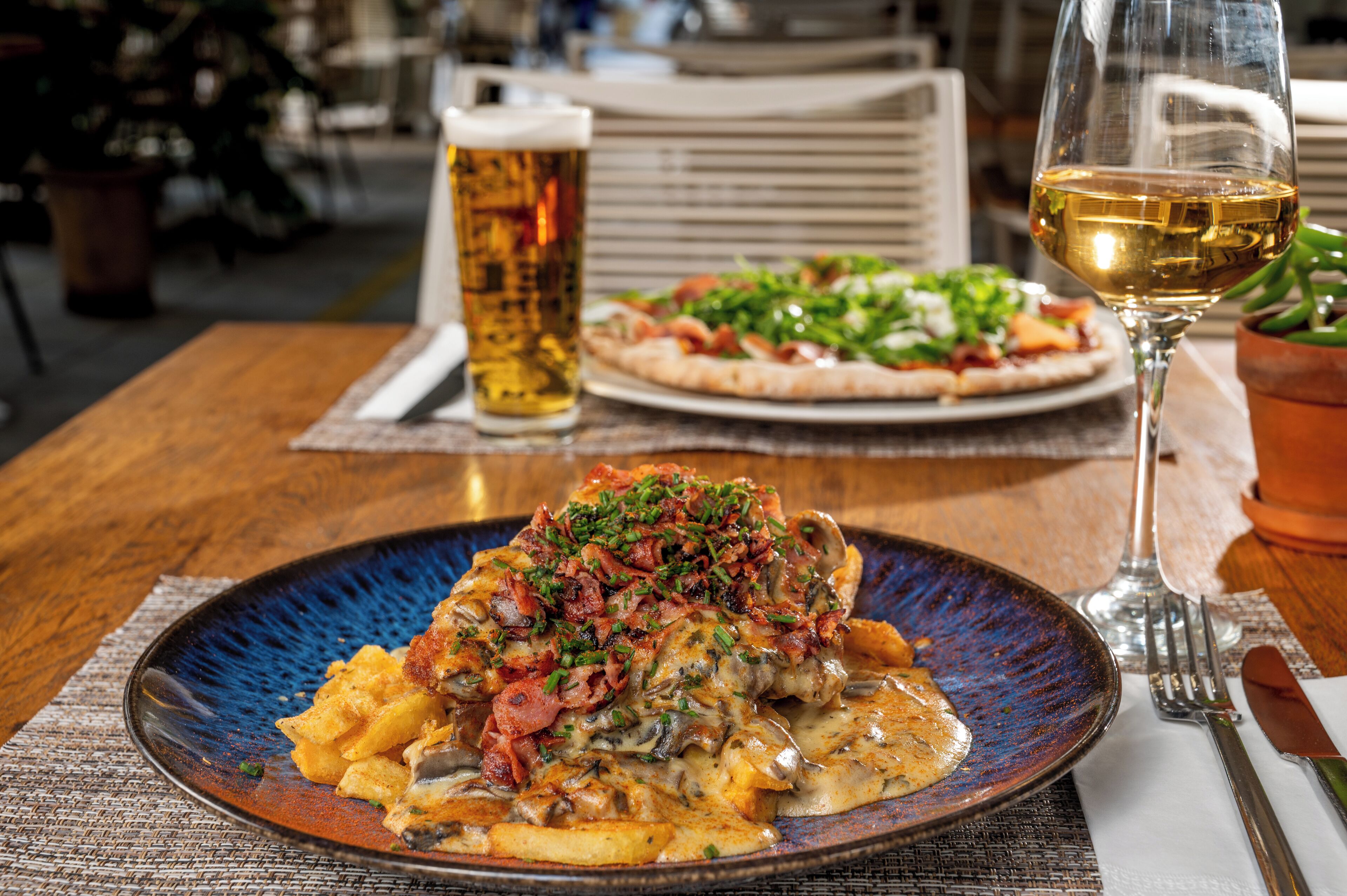 A dining table with a plate of food, a glass of beer, and a glass of wine.