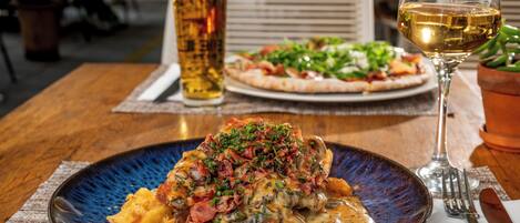 A dining table with a plate of food, a glass of beer, and a glass of wine.