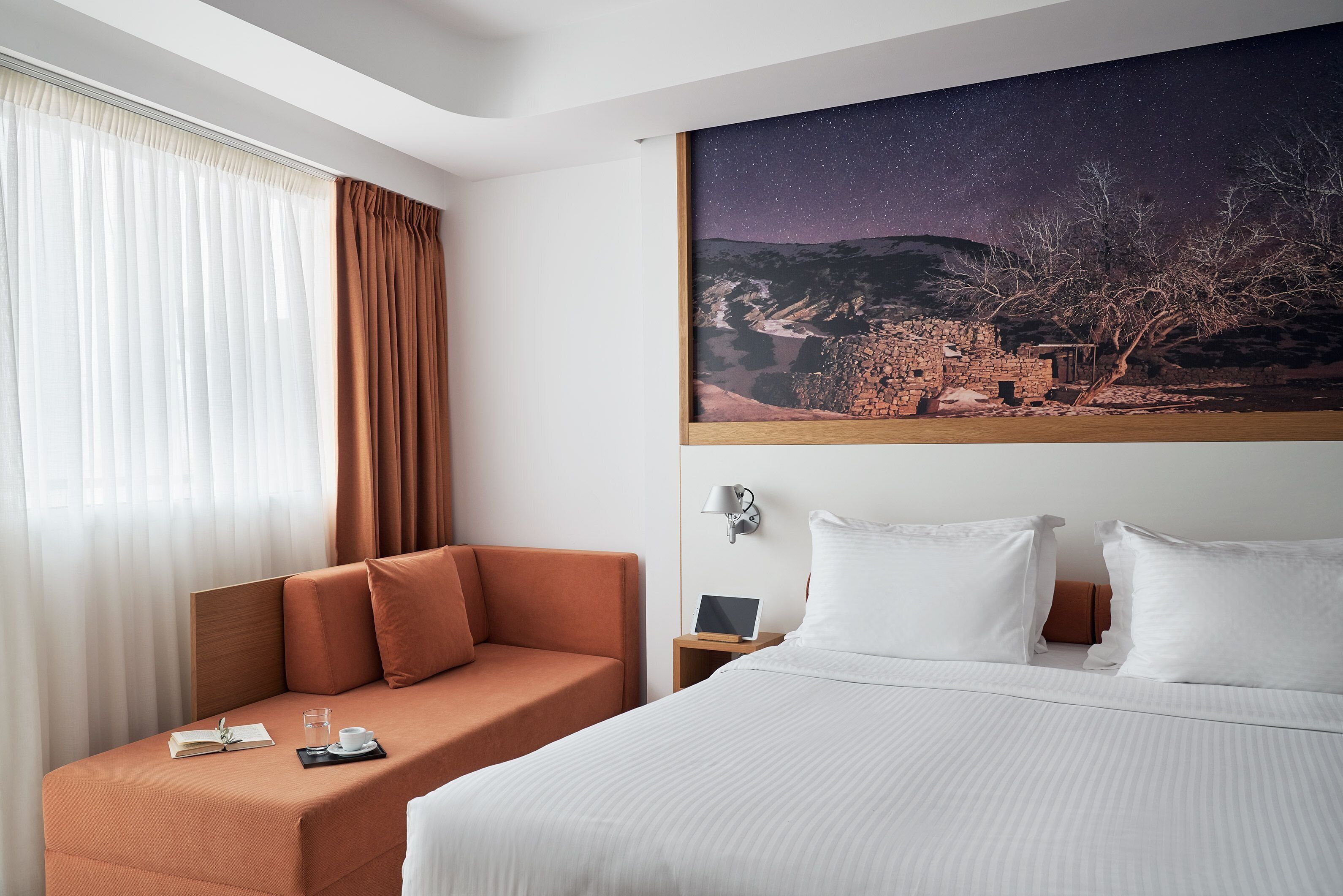 A hotel room with a bed, a sofa, a nightstand with a lamp, and a starry night sky mural on the wall.
