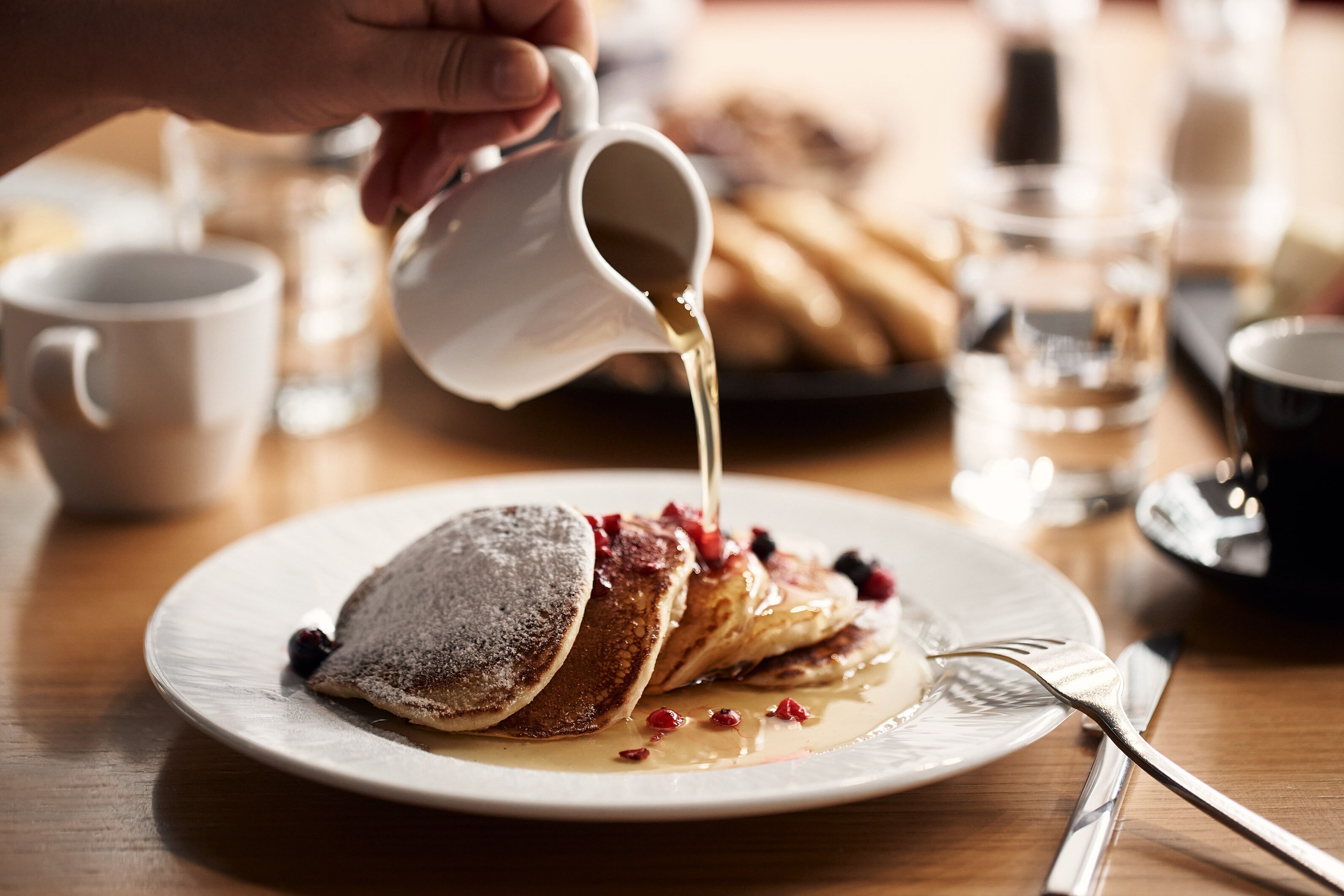 A breakfast setting with pancakes, syrup, and berries on a plate.