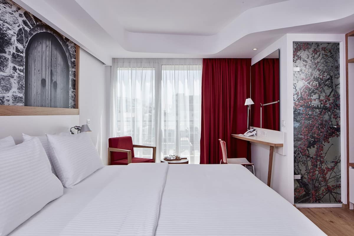 Une chambre d’hôtel avec un grand lit, un bureau, une chaise et une vue sur la ville.