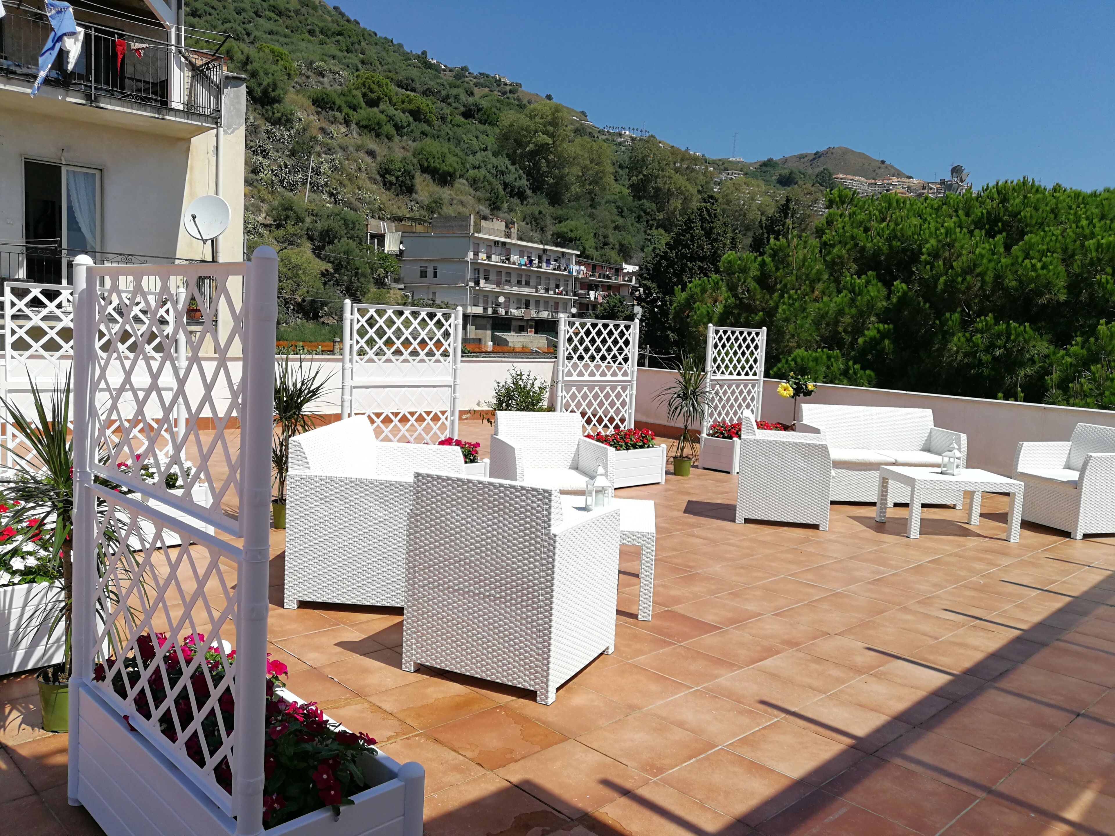Una veranda esterna con mobili in rattan bianco, un pannello decorativo bianco a griglia e fiori rossi.
