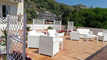 Una veranda esterna con mobili in rattan bianco, un pannello decorativo bianco a griglia e fiori rossi.